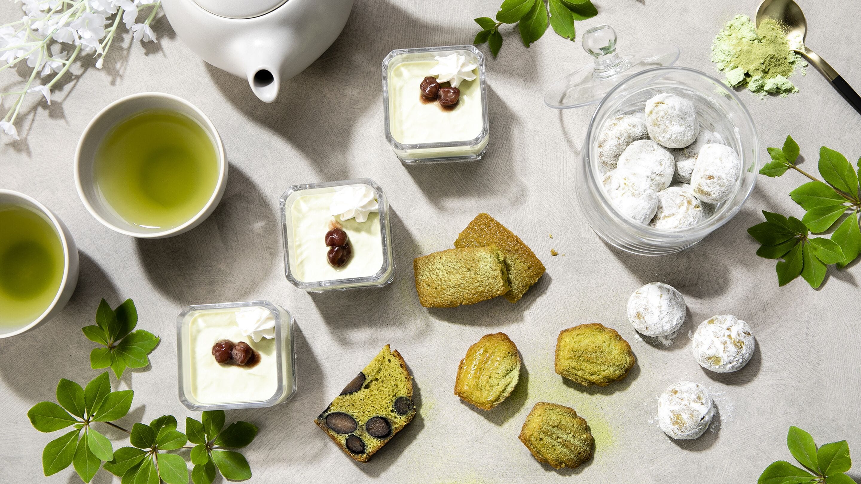 A table with a teapot, cups, desserts, and a glass container.