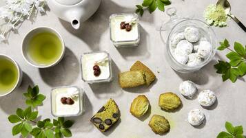 A table with a teapot, cups, desserts, and a glass container.