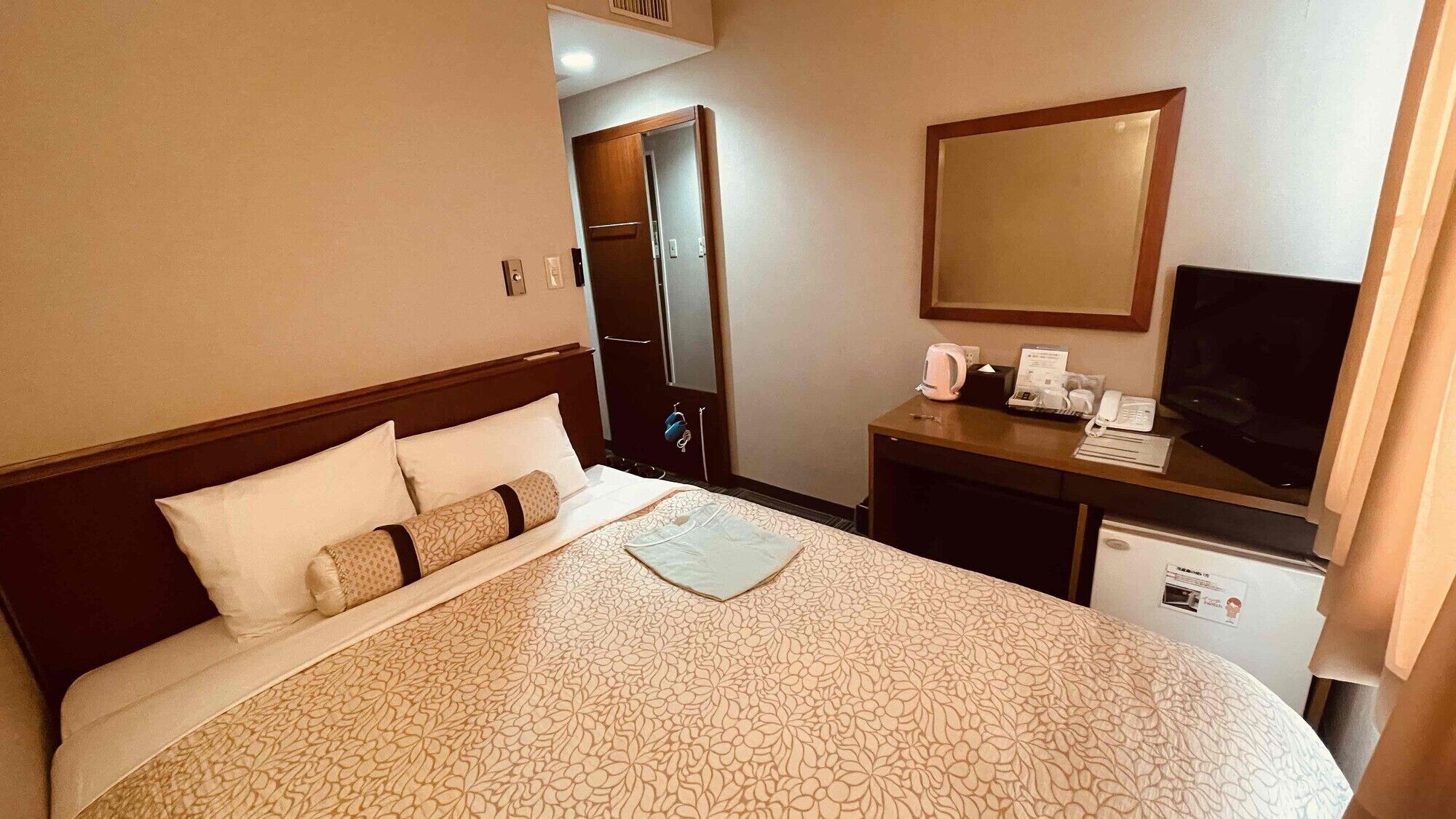 Une chambre d’hôtel équipée d’un lit, d’un bureau avec un ordinateur, d’une télévision et d’un petit réfrigérateur.