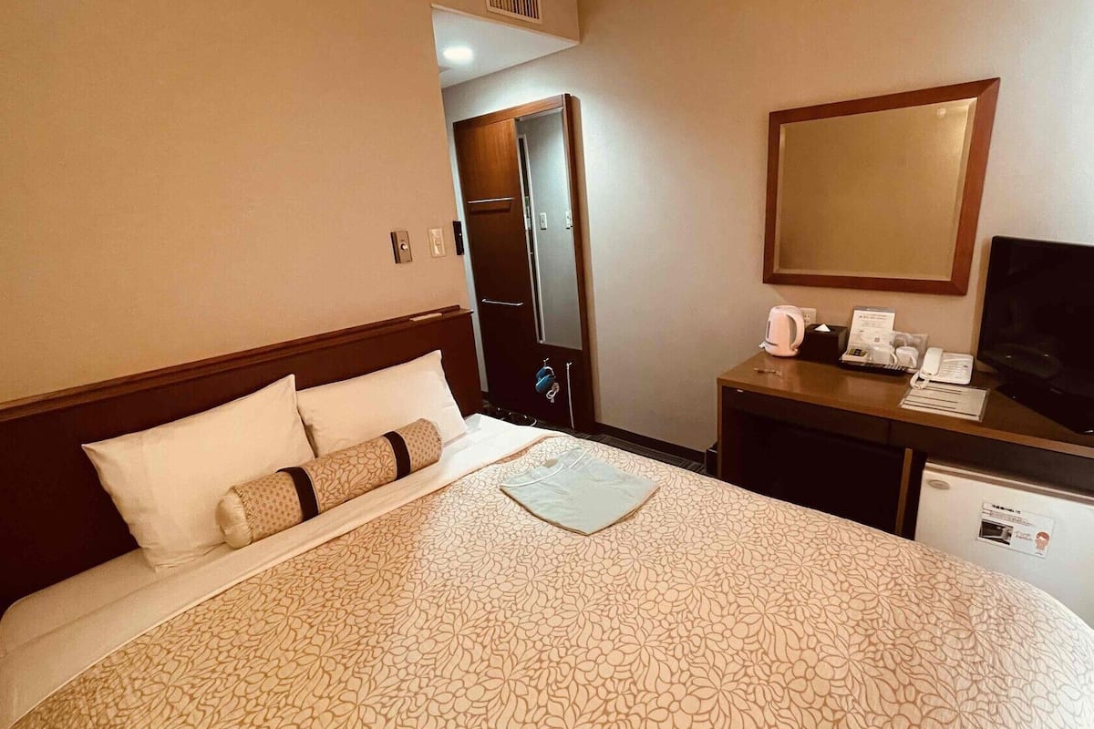 A hotel room with a bed, a desk with a computer, a television, and a small refrigerator.