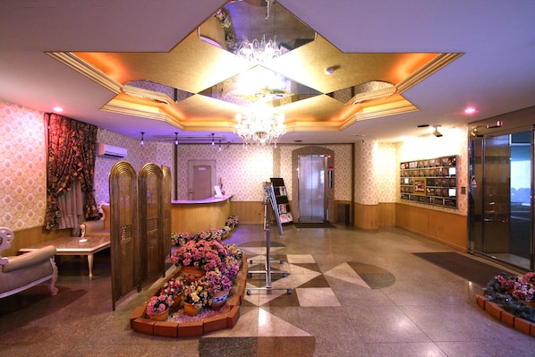 A hotel lobby with a reception desk, a chandelier, a wall-mounted display, and a patterned floor.