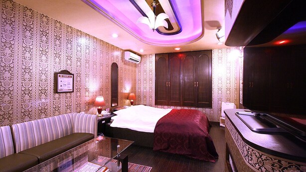 Quarto de hotel com cama, sofá, televisão e minibar.