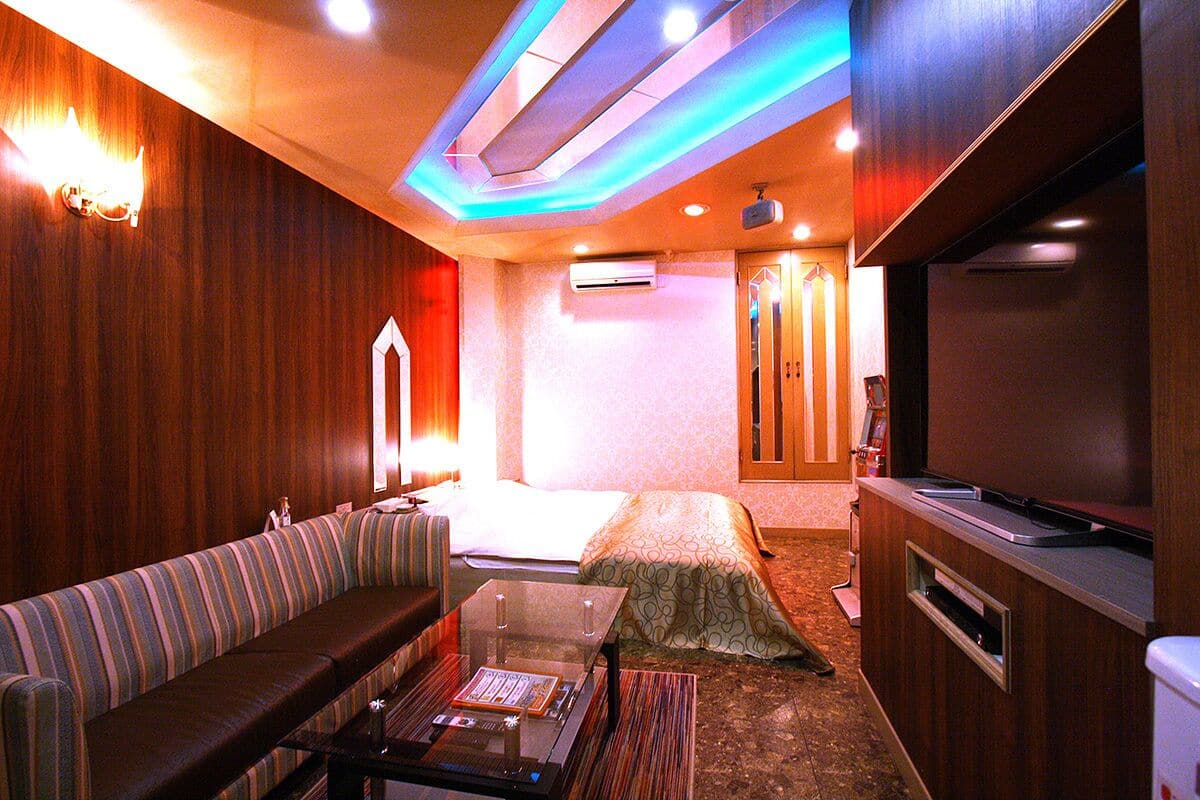 Habitación de hotel con sofá, una mesita, cama, televisión y aire acondicionado instalado en la pared.