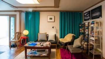 Una sala de estar con piso de madera, una mesa de centro con revistas, una estantería y cortinas color turquesa.