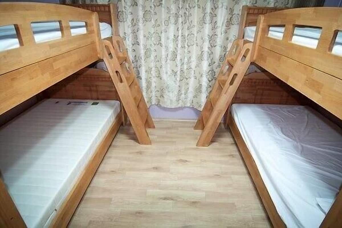 Quarto com duas beliches, piso de madeira e cortina estampada com flores.