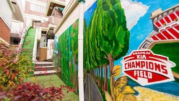 Un mural de un paisaje exuberante con árboles y un estadio identificado como "GWANGJU KIA CHAMPIONS FIELD".