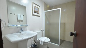 Un baño con lavamanos blanco, inodoro y cabina de ducha con mampara de vidrio.