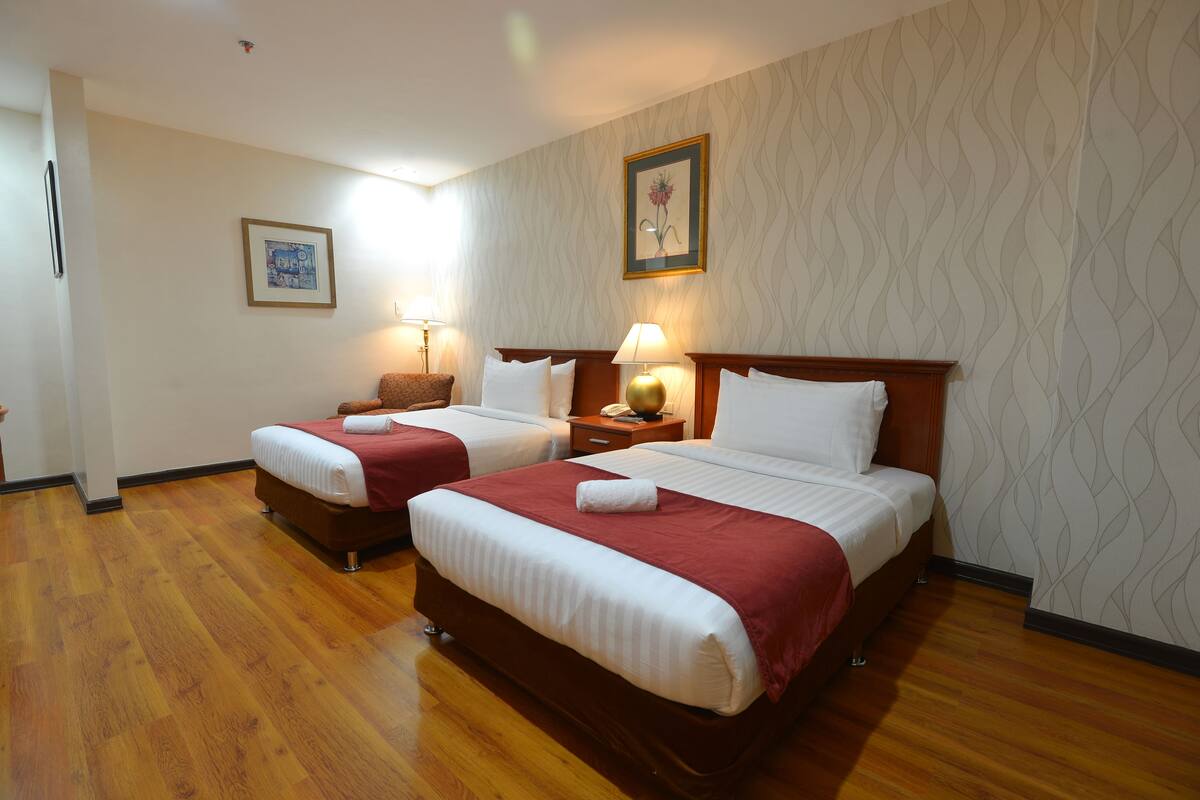 A hotel room with two beds, wooden flooring, and patterned wallpaper.