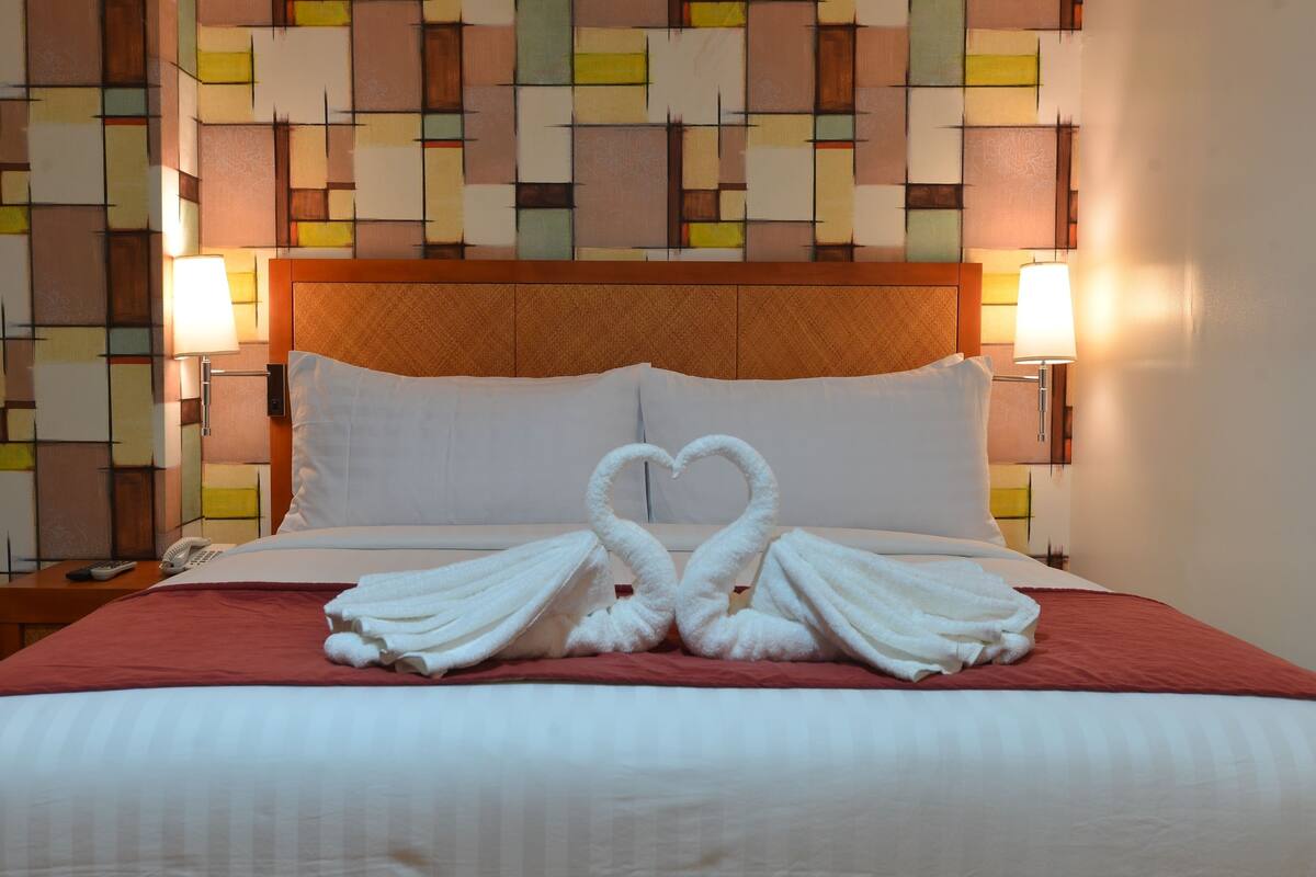 A hotel room with a bed, two wall-mounted lamps, and a geometric-patterned wall.