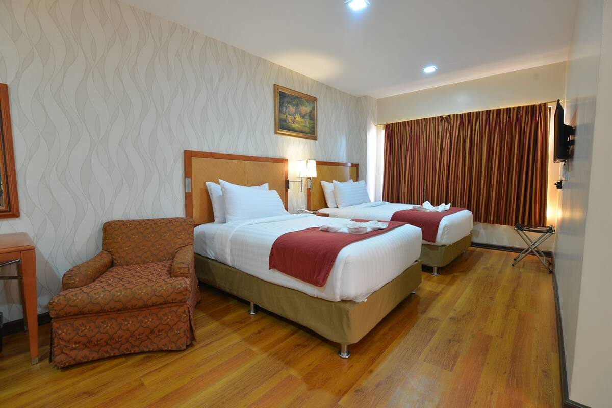 A hotel room with two beds, a chair, a desk, and a television.