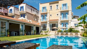 Una piscina con sillas de descanso y sombrillas, rodeada de edificios con balcones y un área de patio techada.
