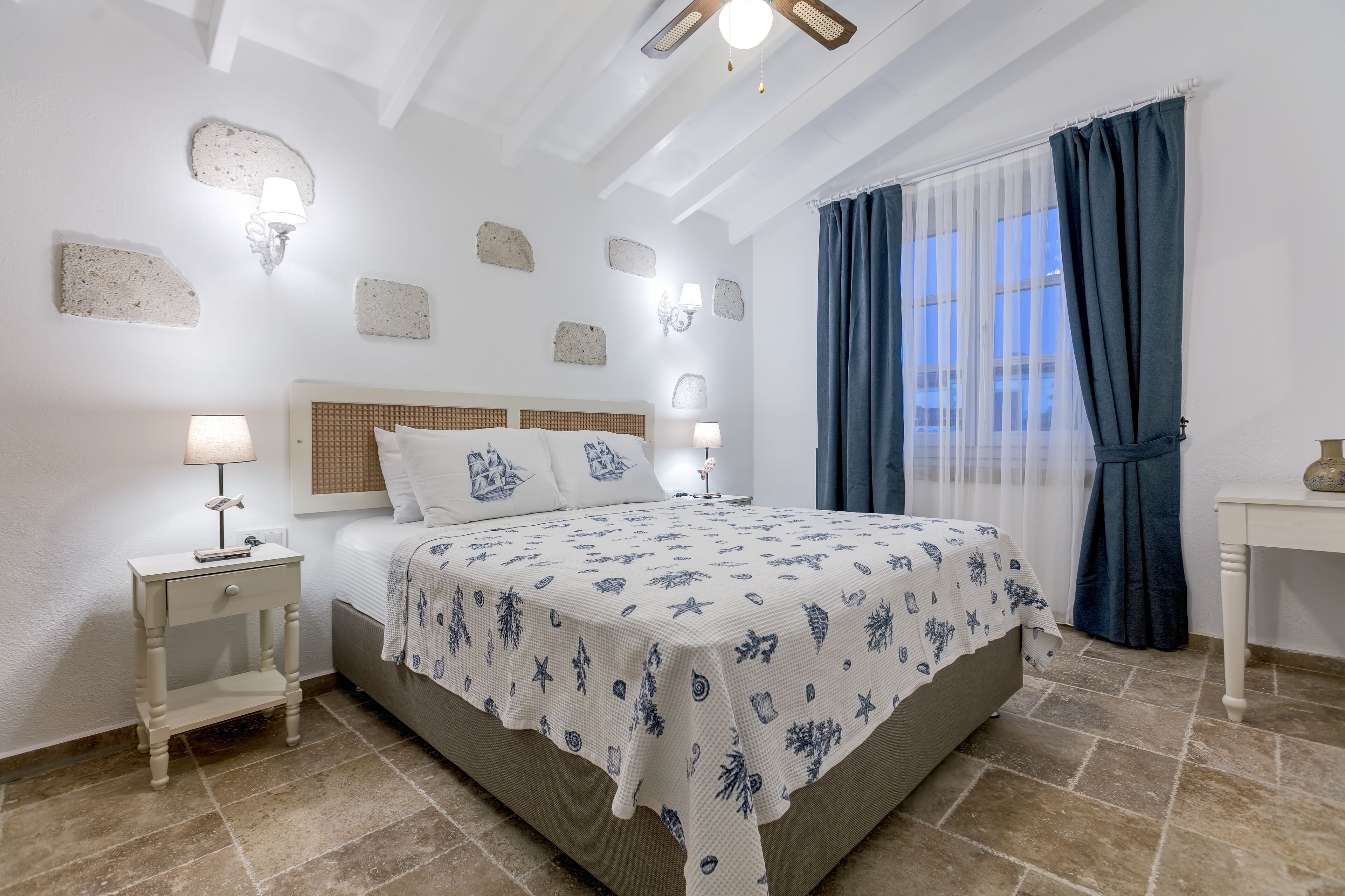 A bedroom with a bed, nightstands, a window with curtains, and wall-mounted lights.