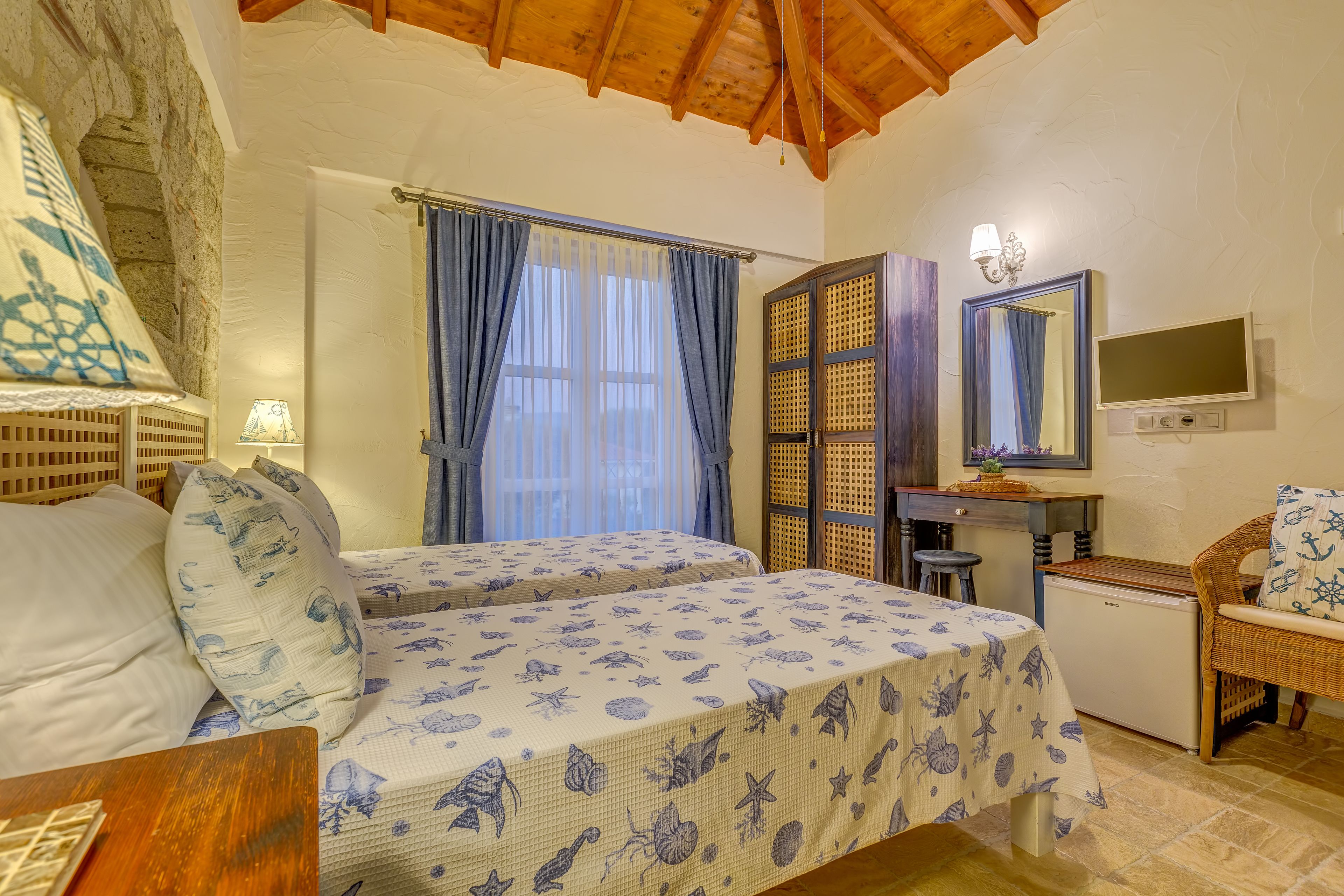 A bedroom with two beds, a desk, a chair, a TV, and a small refrigerator.