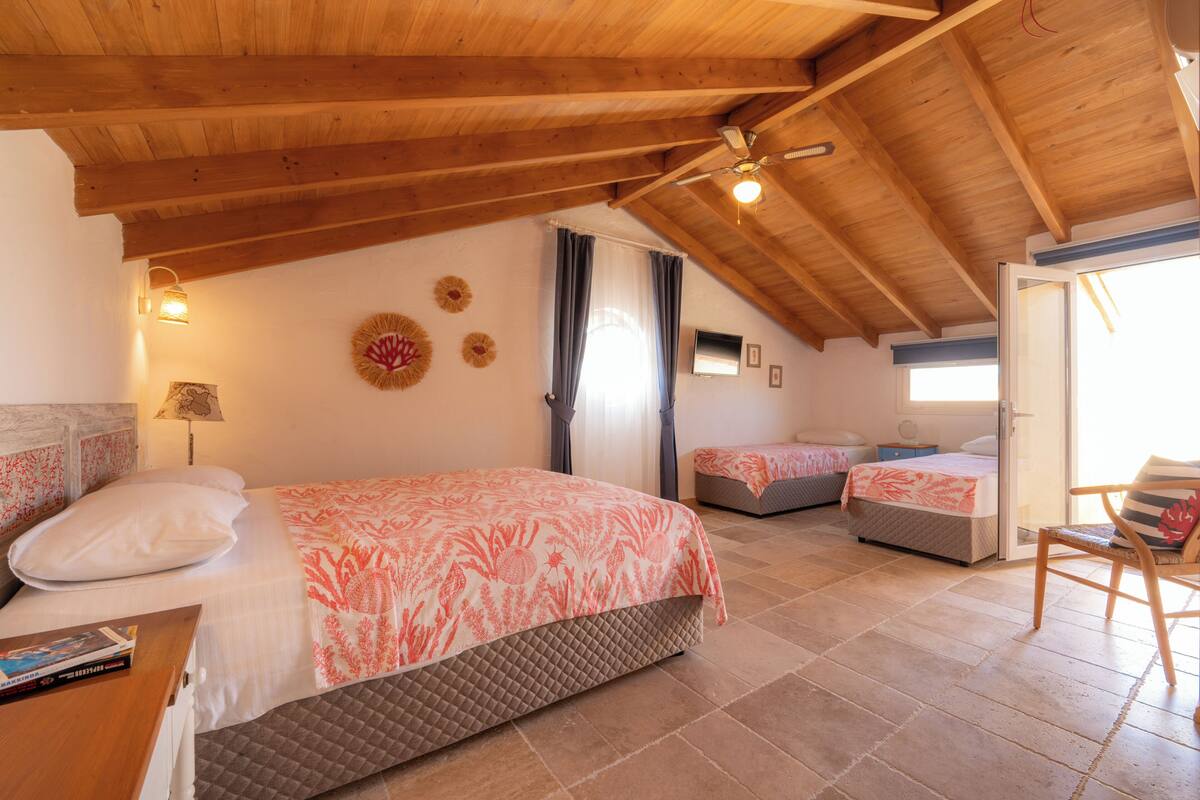 Un dormitorio acogedor en el ático, con techo inclinado, dos camas con ropa de cama floral, una silla de madera y una mesita con un libro.