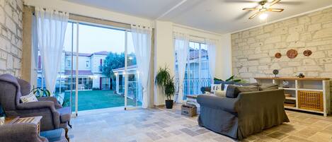 A spacious living area with a large sliding glass door leading to a patio, a ceiling fan, and a stone wall.