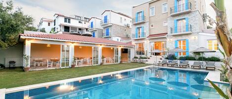 A swimming pool with a covered patio area, surrounded by multi-story buildings with balconies and outdoor seating.