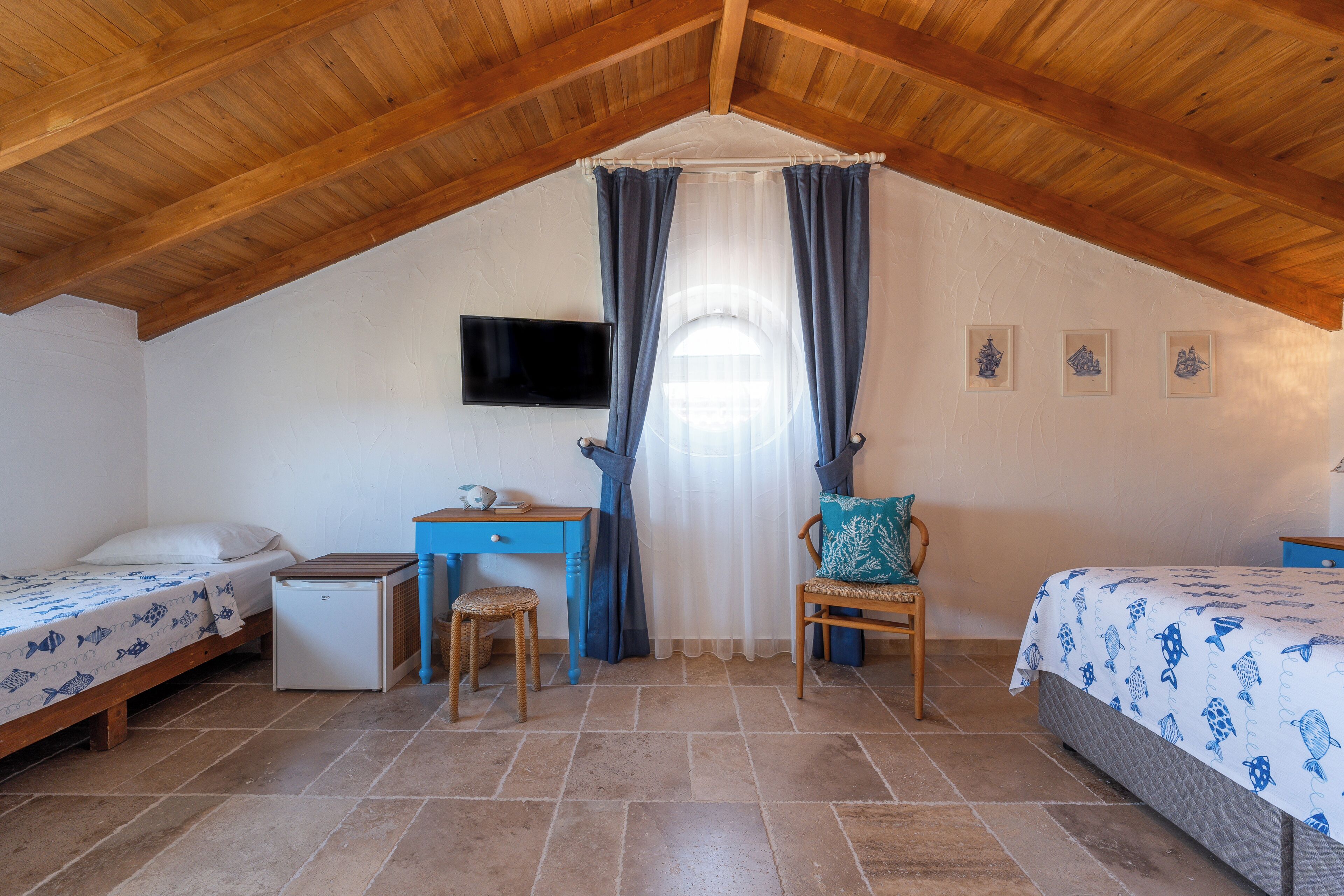 Une chambre mansardée agréable, dotée de deux lits, d’un bureau, d’une chaise et d’un téléviseur.