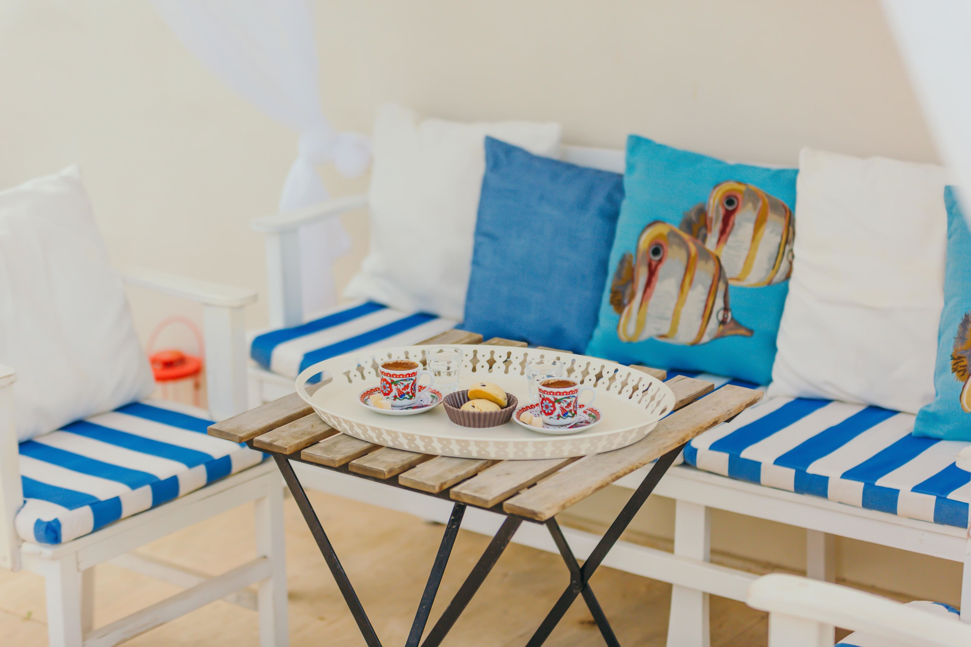 A beachside seating area with a wooden table, blue-striped cushions, and a tray with cups and cookies.