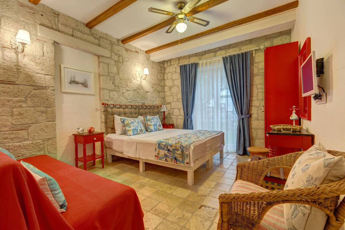 Una habitación acogedora con pared de piedra, cama con colcha estampada, una silla de mimbre y un armario rojo.