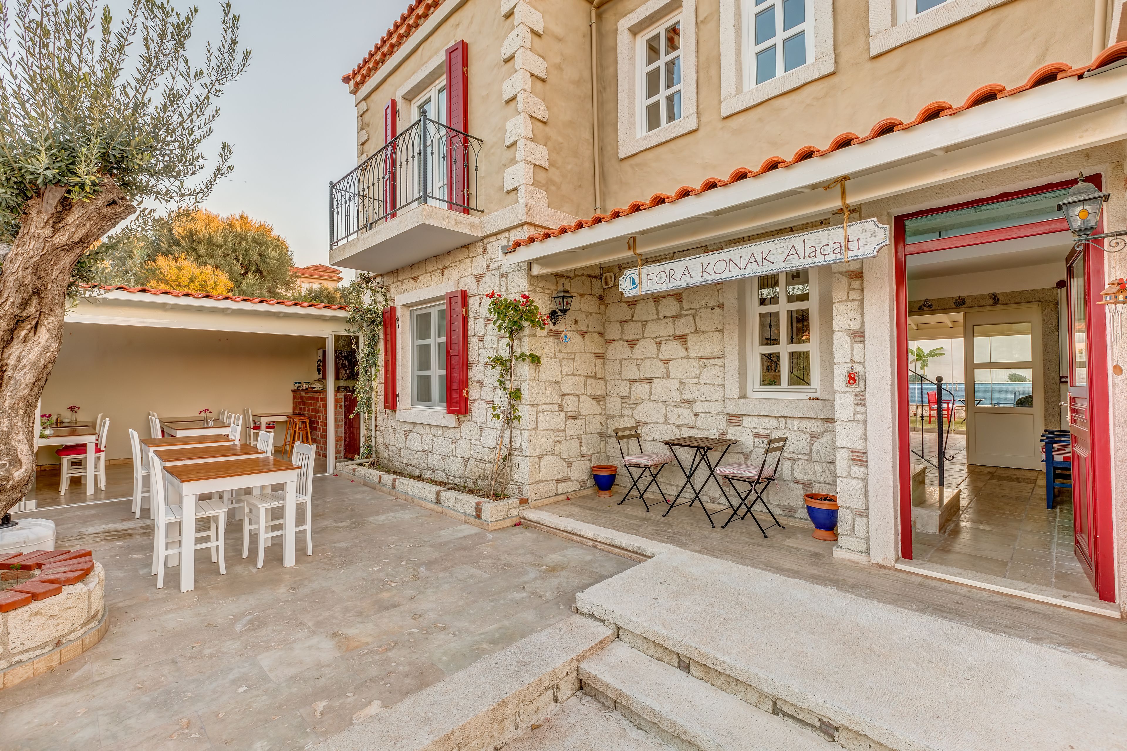 A stone building with a balcony, outdoor seating, and a sign reading "Fora Konak Alacati".