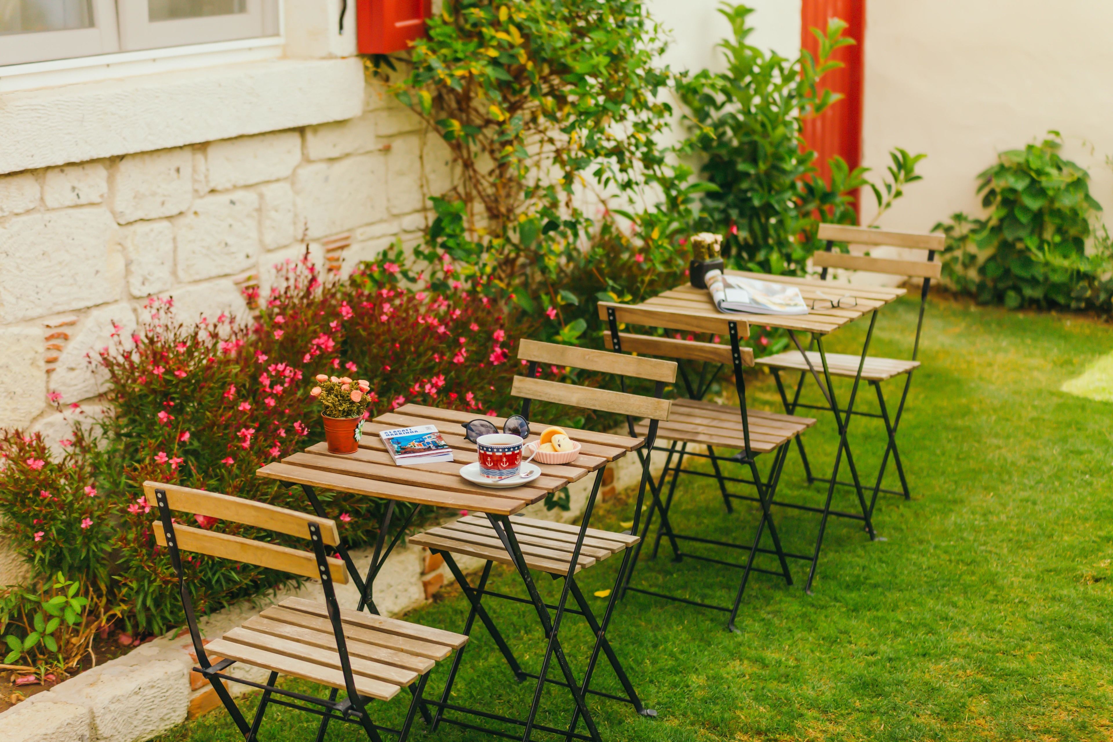 A row of wooden tables and chairs set up outdoors with a brick wall and greenery in the background.