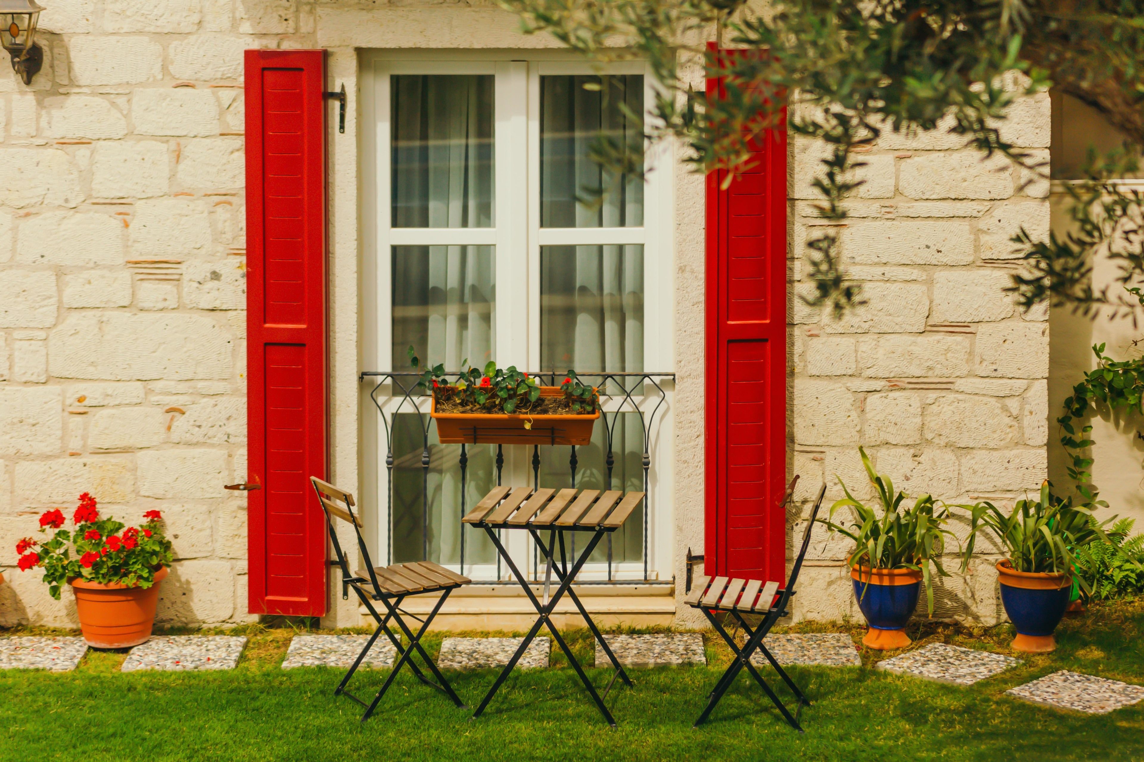 A small outdoor seating area with a table and two chairs, a hanging planter with flowers, and potted plants on a stone pathway.