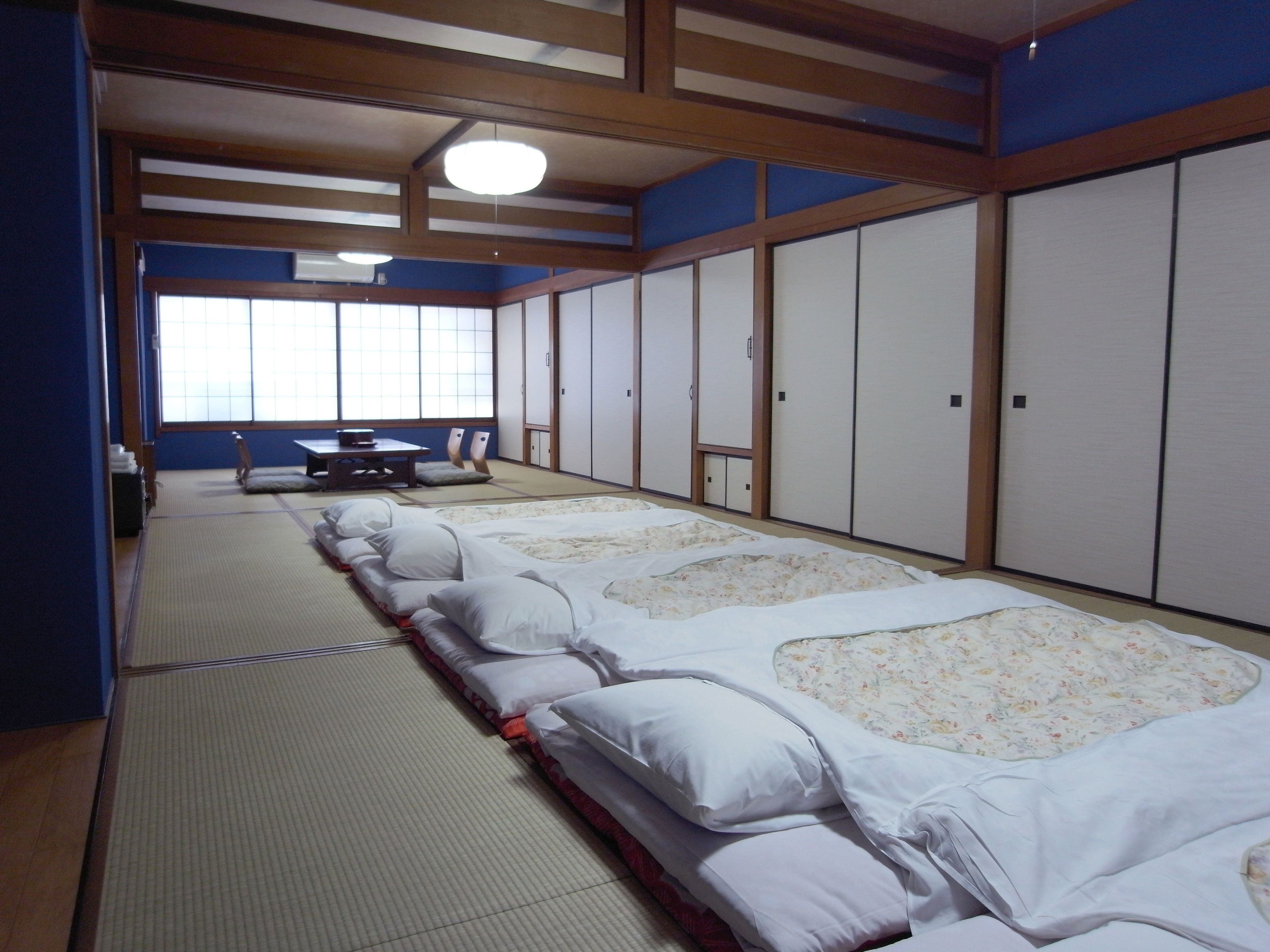 A traditional Japanese room with tatami flooring, a futon bed, sliding doors, and a view of the outside through a window.