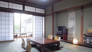 A traditional Japanese room with tatami flooring, a low table with cushions, a television on a stand, and a sliding door leading to a balcony. - Ryokan Yamamuro (Kanazawa)