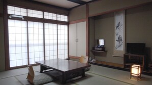 A traditional Japanese room with tatami flooring, a low table, a chair, a TV, and a sliding door. - Ryokan Yamamuro (Kanazawa)