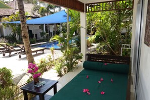 Área da piscina com uma espreguiçadeira verde, uma mesa de madeira com um vaso de flores e um guarda-sol azul oferecendo sombra.