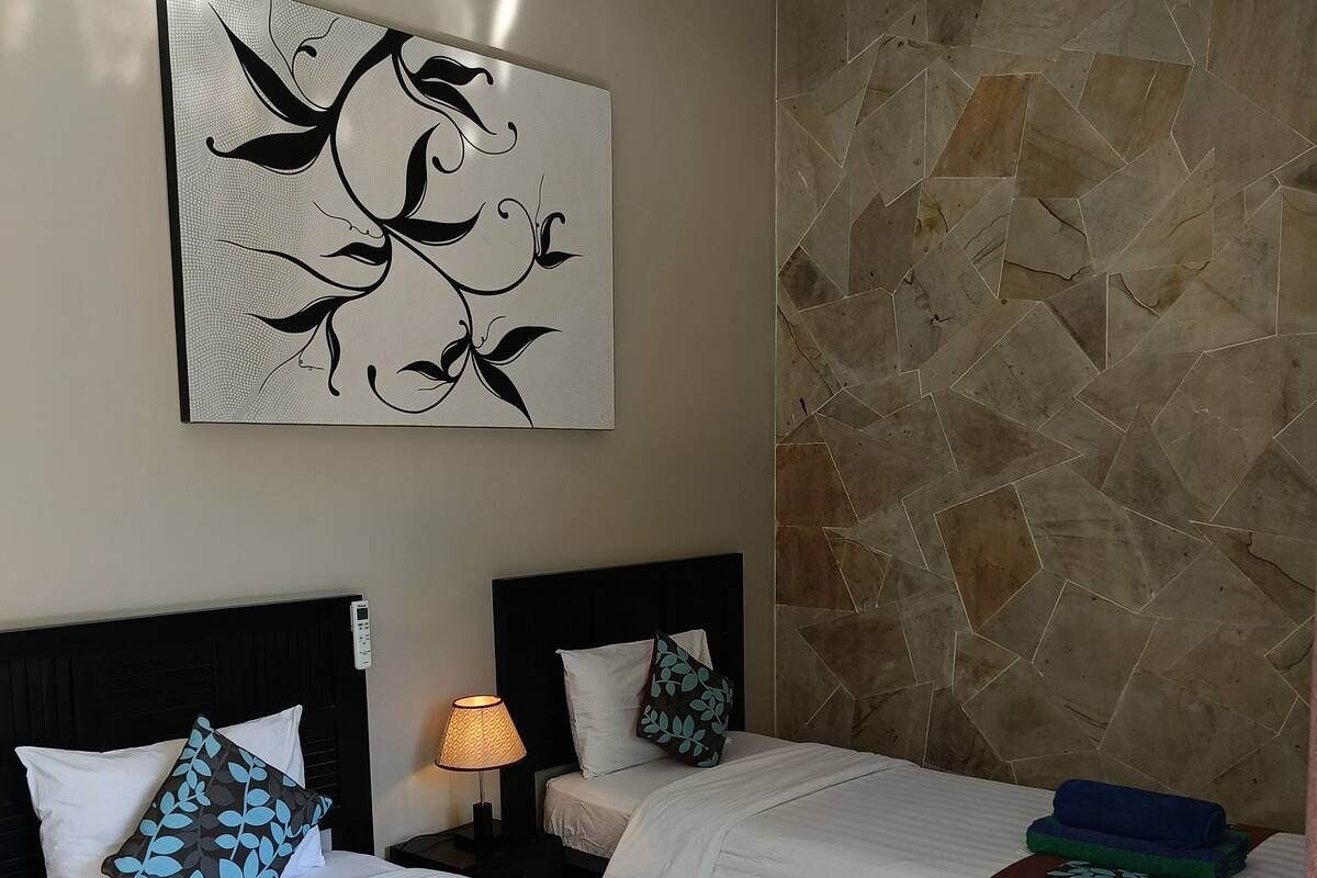 A hotel room with two beds, a large abstract artwork on the wall, and a stone-patterned wall.