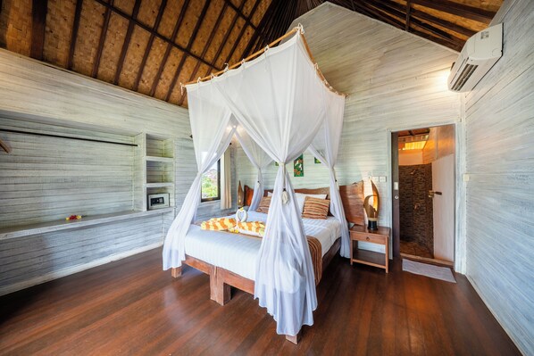 A room with a wooden ceiling, a bed with a canopy, a nightstand, and a door leading to another room. - Abian Huts Dream Beach Lembongan (Lembongan Island)