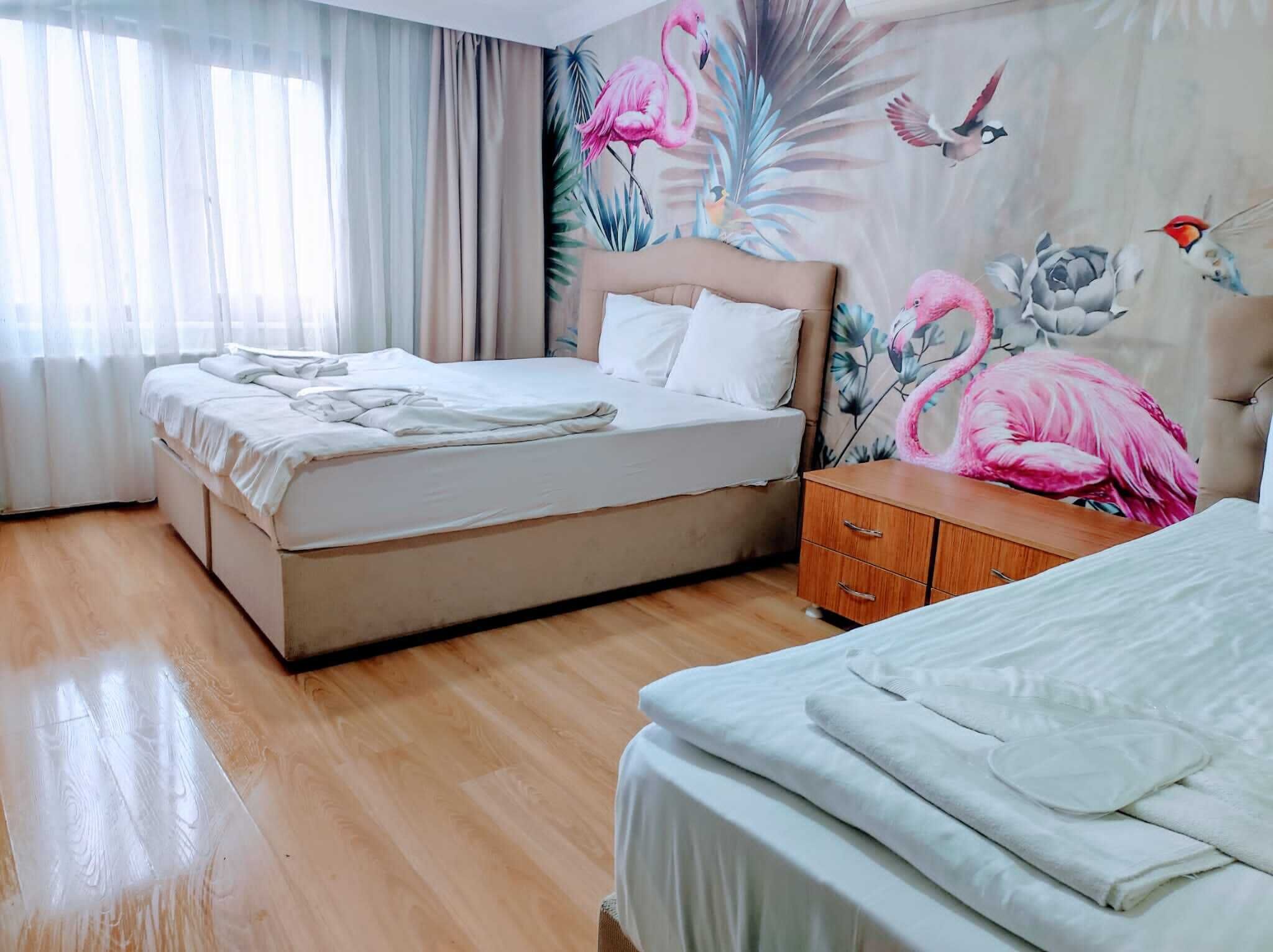 A hotel room with a bed, a wooden nightstand, and a wall with a tropical mural.