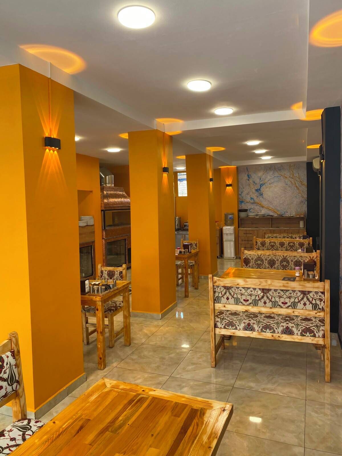 A restaurant with wooden furniture, recessed ceiling lights, and a marble backsplash.