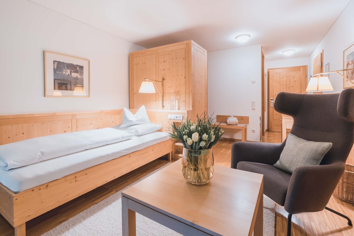 A room with a wooden bed, a sofa, a table with a vase of flowers, and a chair.