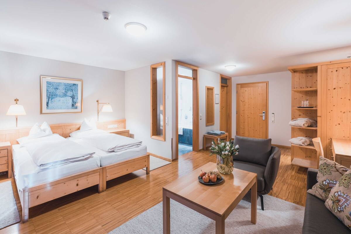A modern hotel room with a wooden bed, a small table with a vase, a grey sofa, and wooden cabinets.