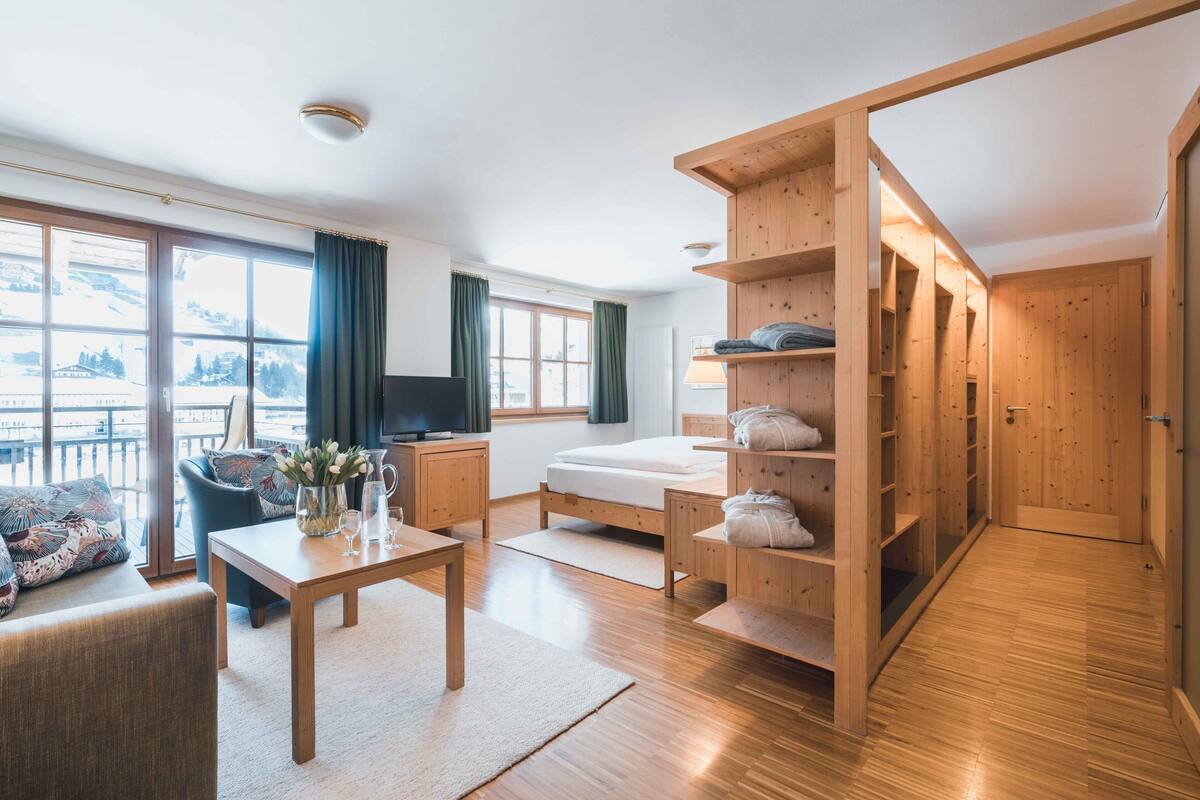 A modern hotel room with a wooden floor, a sofa, a TV, a bed, a desk, and a wardrobe.