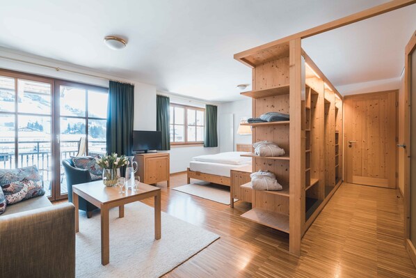 A modern hotel room with a wooden floor, a sofa, a TV, a bed, a desk, and a wardrobe. - Felbermayer Hotel & AlpineSpa - Montafon (Gaschurn)