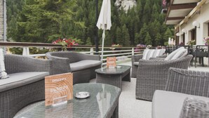 Un espace extérieur aménagé avec des meubles en osier, une table en verre sur laquelle est posé un menu de desserts, et une vue sur une zone boisée.