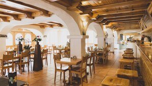 Un restaurant spacieux avec des tables et des chaises en bois, de hauts plafonds avec des poutres apparentes et de grandes fenêtres laissant entrer la lumière naturelle.