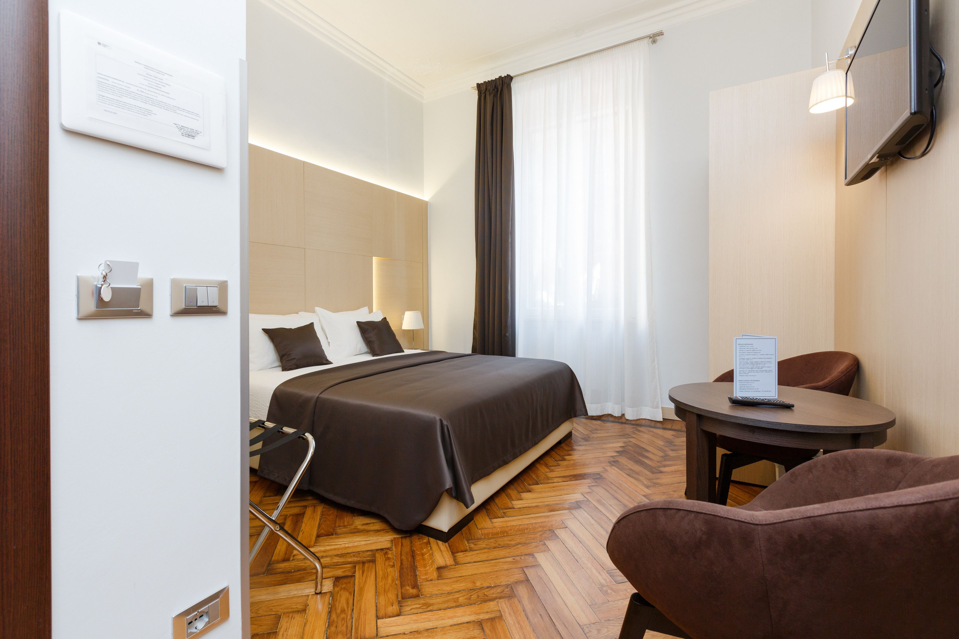 A hotel room with a bed, a desk, a chair, and a window with curtains.