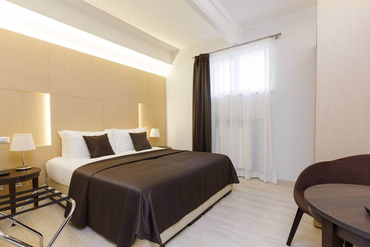 A modern hotel room with a large bed, bedside tables, a desk, and a chair.