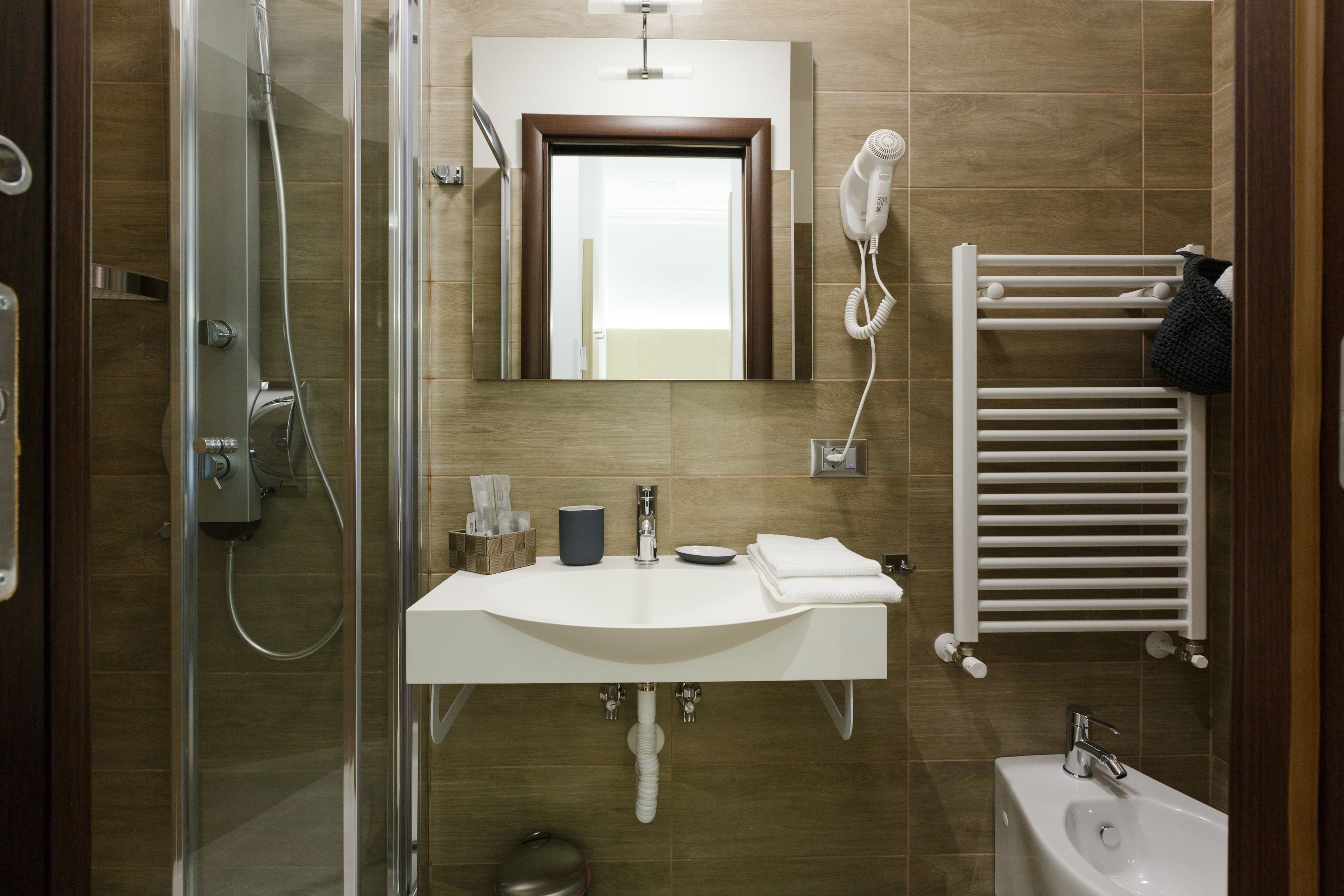 A modern bathroom with a glass shower enclosure, a white sink with a mirror above, and a white towel rack.