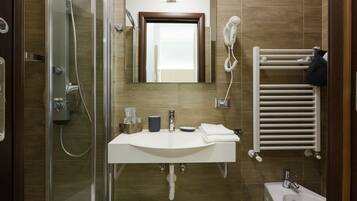 A modern bathroom with a glass shower enclosure, a white sink with a mirror above, and a white towel rack.