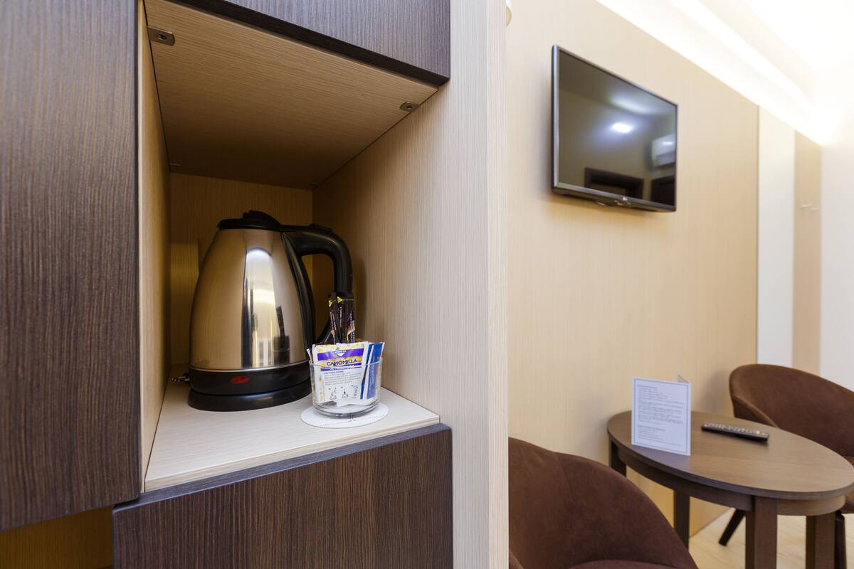 A compact kitchenette with a kettle, a coffee maker, and a small table with a remote control and a menu.