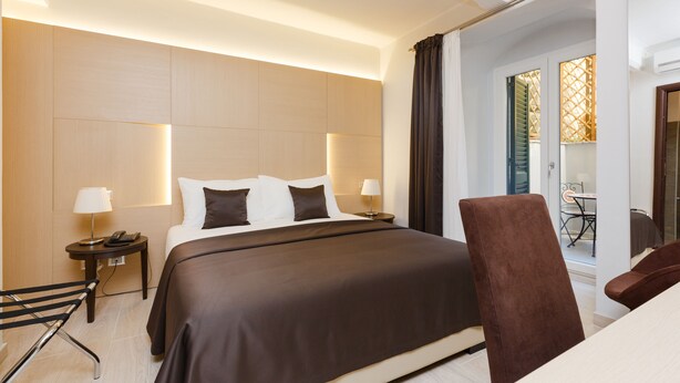 A hotel room with a large bed, two bedside tables with lamps, a chair, and a view of the outside. - Domus Terenzio (Rome)