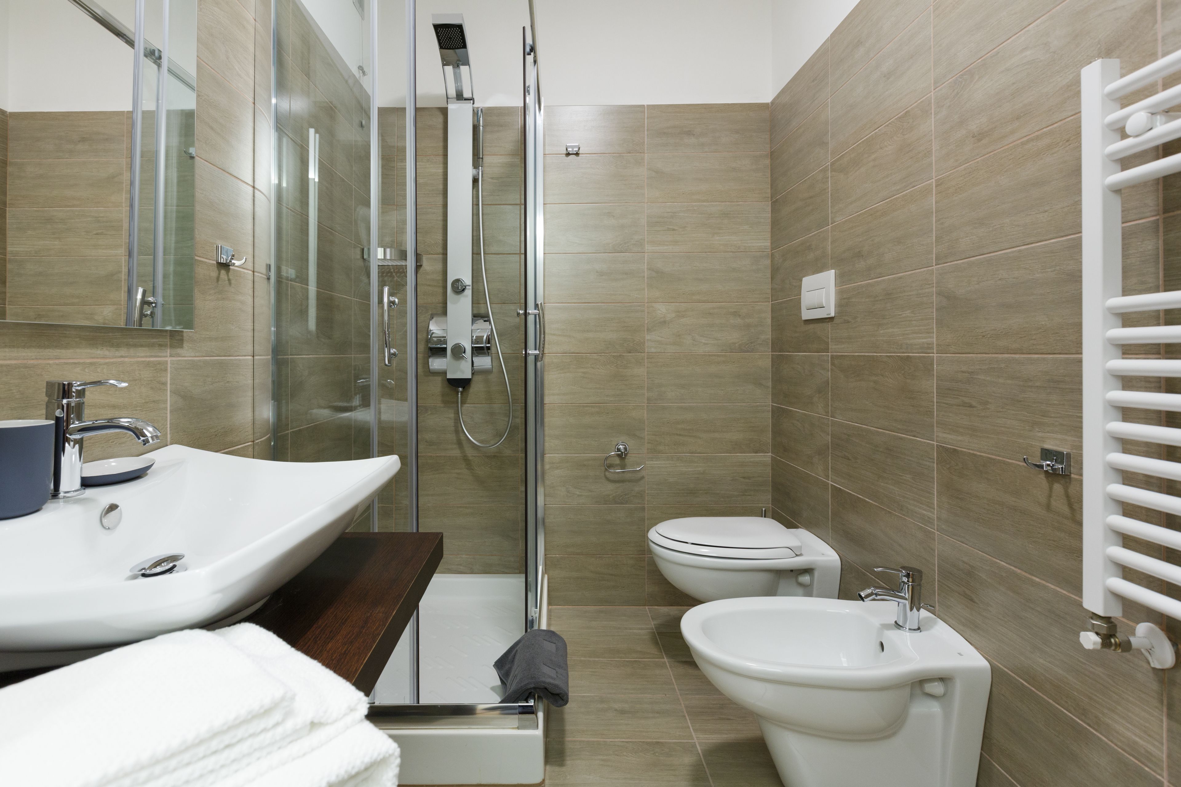 A modern bathroom with a shower, two sinks, a toilet, and a towel rack.