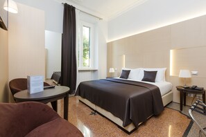 A hotel room with a bed, a desk, a chair, a window with curtains, a lamp, and a sign. - Domus Terenzio (Rome)