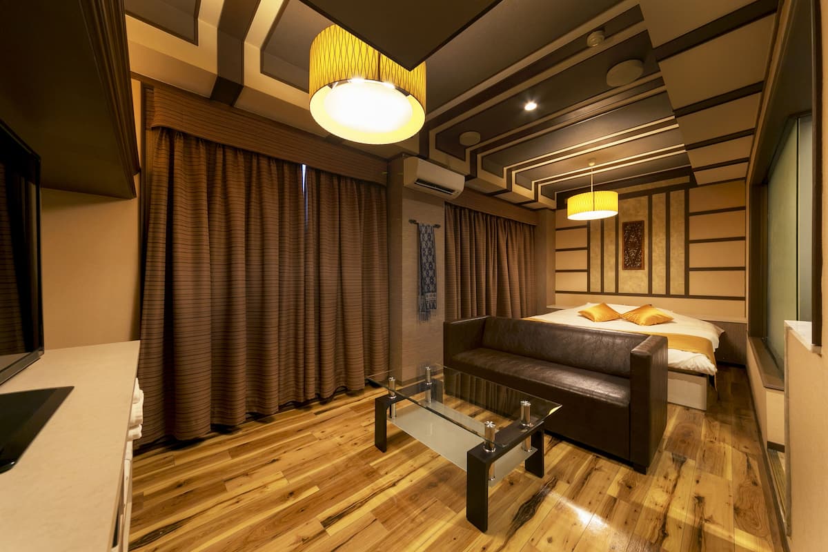 Ein modernes Hotelzimmer mit Holzboden, einem Glastisch, einer Couch, einem Bett mit Kissen und einem großen Fenster mit Vorhängen.