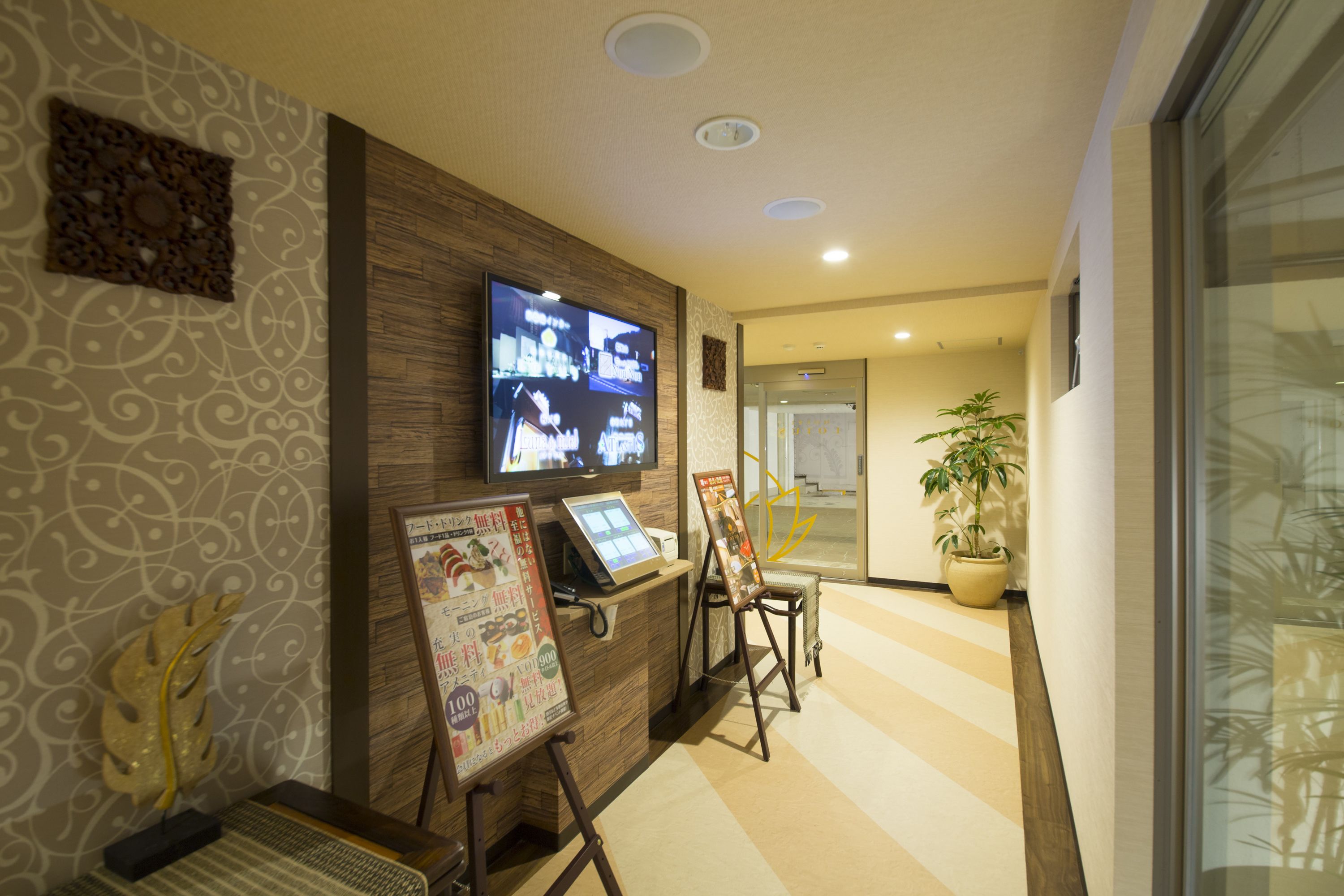 Un área de recepción con un mostrador de madera, un televisor montado en la pared y una planta en maceta.